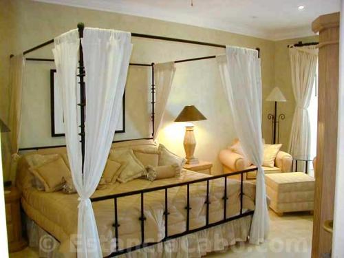 the master bedroom features a king size canopy bed with lovely white draped fabric.